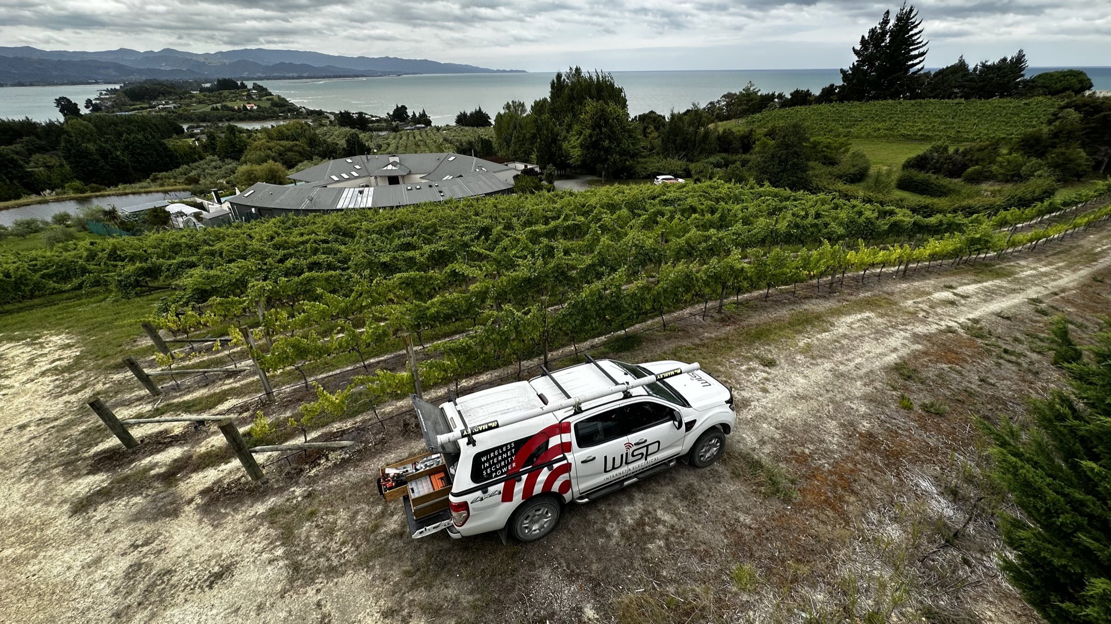WISP Electrical ute parked at a Tasman vineyard with the bay in the background